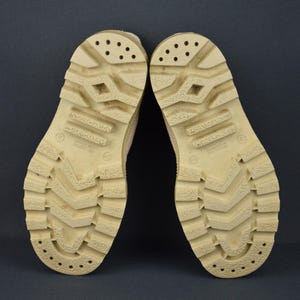 Puede incluir: Un par de botas de cuero color beige con una suela gruesa de goma. Las suelas tienen un patr&oacute;n de banda de rodadura y est&aacute;n marcadas con la palabra "Imitation".