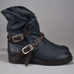 May include: Dark blue leather ankle boots with brown straps and silver buckles. The straps have decorative studs.