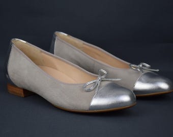 May include: A pair of gray suede ballet flats with silver toe caps and bows. The flats have a low heel.