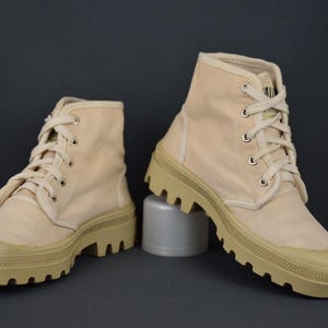 Puede incluir: Un par de botas altas de lona beige con suelas gruesas y robustas. Las botas tienen cierre de cordones y est&aacute;n hechas de una tela suave y transpirable.