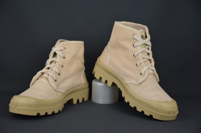 Puede incluir: Un par de botas altas de lona beige con suelas gruesas y robustas. Las botas tienen cierre de cordones y est&aacute;n hechas de una tela suave y transpirable.