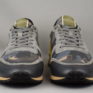 Puede incluir: Par de zapatillas grises y camuflaje con suelas negras y detalles beige. Las zapatillas tienen cordones grises y el nombre de la marca es visible en la leng&uuml;eta. Los zapatos est&aacute;n dise&ntilde;ados para uso casual.