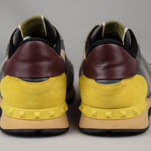 Puede incluir: Par de zapatillas deportivas grises, amarillas y burdeos. El tal&oacute;n presenta un panel de cuero burdeos, y los laterales son grises con detalles de ante amarillo. Las suelas son color canela con suelas negras y detalles tachonados. Las zapatillas son para uso casual.