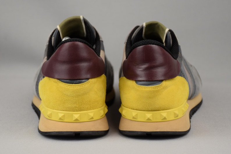 Puede incluir: Par de zapatillas deportivas grises, amarillas y burdeos. El tal&oacute;n presenta un panel de cuero burdeos, y los laterales son grises con detalles de ante amarillo. Las suelas son color canela con suelas negras y detalles tachonados. Las zapatillas son para uso casual.