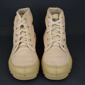 Puede incluir: Un par de zapatillas de lona de color blanco roto de ca&ntilde;a alta con cordones blancos. Las zapatillas tienen suela de goma y un logotipo negro en el lateral.