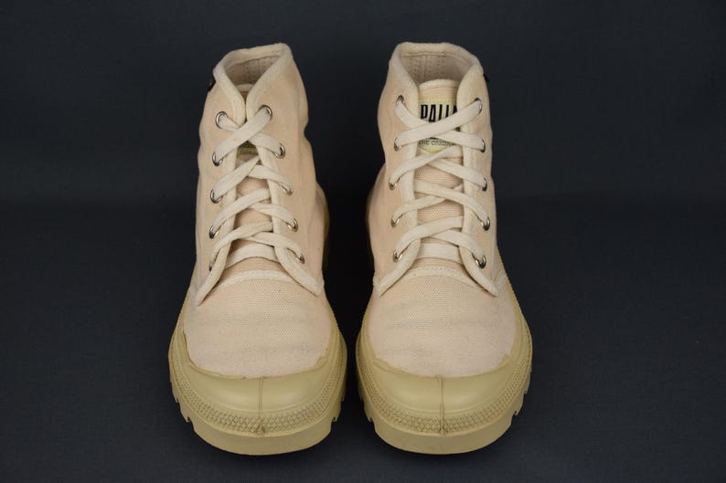 Puede incluir: Un par de zapatillas de lona de color blanco roto de ca&ntilde;a alta con cordones blancos. Las zapatillas tienen suela de goma y un logotipo negro en el lateral.