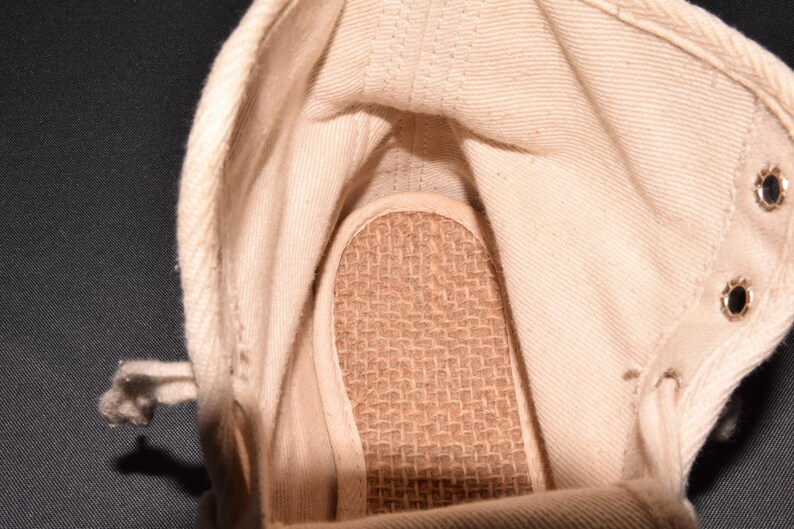 Puede incluir: El interior de una zapatilla de lona blanca con una plantilla tejida marr&oacute;n.