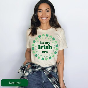 May include: A beige t-shirt with a green shamrock design and the text "in my Irish era".