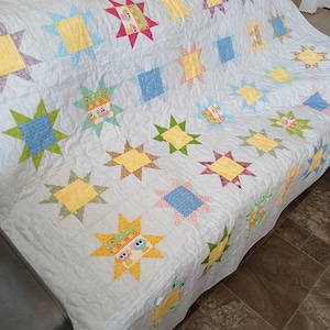 May include: A handmade quilt with a repeating star design. The stars are made from a variety of colourful fabrics, including yellow, blue, green, and red. The quilt is draped over a sofa, highlighting its design and craftsmanship.