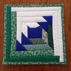 Peut inclure: Un carré de courtepointe patchwork vert et bleu avec un centre blanc et un motif en spirale.