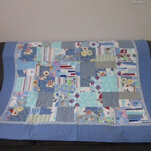 May include: A patchwork quilt with a blue background and a variety of colourful patterns, including stars, stripes, and animals. The quilt is made of different fabrics and textures, and it has a white border.