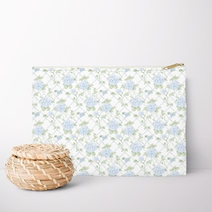 Puede incluir: Una bolsa blanca con cremallera con un patrón repetitivo de flores azules y enredaderas verdes sobre un fondo blanco.