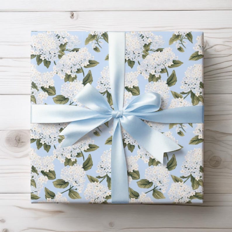 May include: A wrapped gift with a light blue floral patterned paper featuring white flowers and green leaves. A light blue satin ribbon is tied in a bow around the gift.