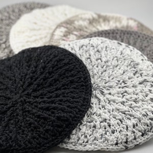 Puede incluir: Un juego de posavasos de ganchillo en varios tonos de gris, negro y blanco. Los posavasos son circulares y tienen un diseño texturizado y tejido.