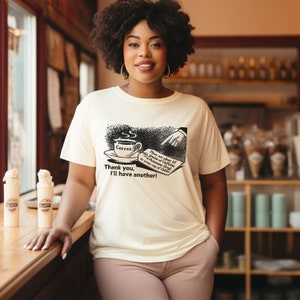 May include: A white t-shirt with a black and white illustration of a cup of coffee and text that reads "There are about 21 grains of Caffeine in every cup of Coffee. Thank you, I'll have another!"