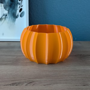 May include: Orange pumpkin-shaped planter with vertical ridges.