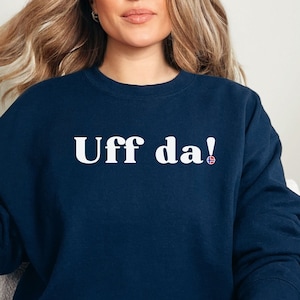 May include: A navy blue sweatshirt with the text "Uff da!" in white lettering and a small Norwegian flag.