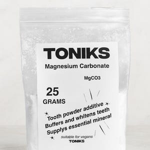 May include: A clear plastic bag containing 25 grams of magnesium carbonate powder, labelled "TONIKS." The label includes the chemical formula MgCO3 and text stating it is a tooth powder additive that buffers and whitens teeth. Suitable for vegans.
