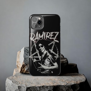 May include: A black smartphone case featuring a white graphic print of a person wearing sunglasses and holding a book, centered over a pentagram symbol. The text RAMIREZ is printed in a distressed white font at the top of the phone case design.