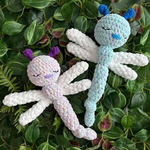 May include: Two crocheted dragonfly toys. One is white with purple accents and the other is blue with white accents.