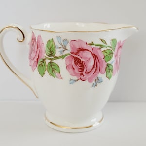 Peut inclure: Crémier de couleur crème avec un motif floral de roses roses. Le crémier a une poignée et une base dorées. Les roses sont d'un rose vif avec des feuilles vertes et des accents bleus. Une pièce classique.