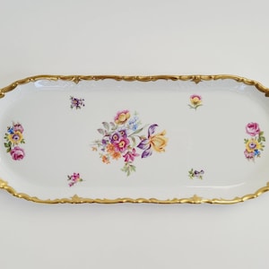 May include: An oval, white porcelain serving platter with a gold-colored, scalloped rim. The platter is decorated with colorful floral arrangements in the center and at each end. The flowers include pink, yellow, purple, and blue blooms.