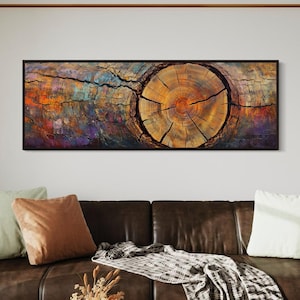 May include: A brown leather sofa with a throw blanket and cushions in front of a wall with a framed abstract painting of a tree trunk cross section. The painting has a colourful background with shades of purple, blue, orange, and yellow.