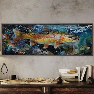 Op de afbeelding: Een ingelijste aquarel van een bruine forel die onder water zwemt. De vis heeft oranje, bruine en gele schubben. Het kunstwerk hangt boven een donkere houten console met een lamp, boeken en decoratieve items.
