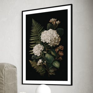 Könnte beinhalten: Ein gerahmter botanischer Druck mit weißen Hortensien und Farnen vor schwarzem Hintergrund. Das Kunstwerk hängt über einem dunklen Nachttisch aus Holz mit einer modernen schwarzen Lampe und einer Vase mit weißen Blumen. Ein Buch liegt auf dem Tisch.