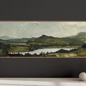 May include: A framed landscape painting depicting a green valley with a lake and a hilltop in the distance. The sky is a soft blue with white clouds. The painting is in a wooden frame.