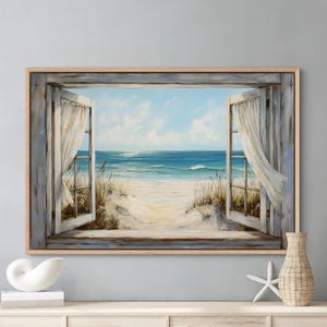 Könnte beinhalten: Ein rechteckiger Wandkunstdruck mit einem offenen Fensterrahmen aus verwittertem grauem Holz, der den Blick auf einen Sandstrand, hohe Dünen Gräser und einen blauen Ozean unter einem bewölkten Himmel freigibt. Weiße, transparente Vorhänge hängen seitlich.