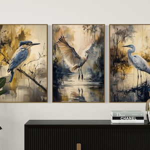 May include: A set of three framed watercolor paintings featuring birds in a nature setting. The paintings are in shades of blue, brown, and white, with a soft, painterly style.
