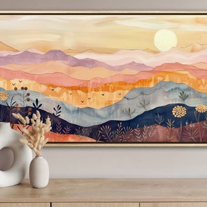 以下が含まれることがあります： 空に太陽が輝く山脈を描いた、額縁に入った抽象画。山はオレンジ、ピンク、パープル、ブルー、グリーンの色合いで描かれている。太陽は明るい黄色の円形である。