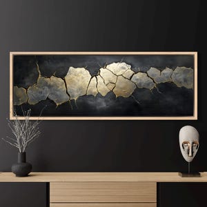 May include: Abstract painting in a wooden frame with a black background and gold and silver cracks. The painting is on a wall above a wooden shelf with a decorative mask on the right side.