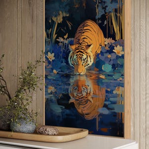 A majestic tiger drinks from a calm lake, its reflection glowing in golden hues. Surrounded by blue flowers and soft light, this art print blends nature with elegance, perfect for boho, nature, or wildlife-themed home decor.