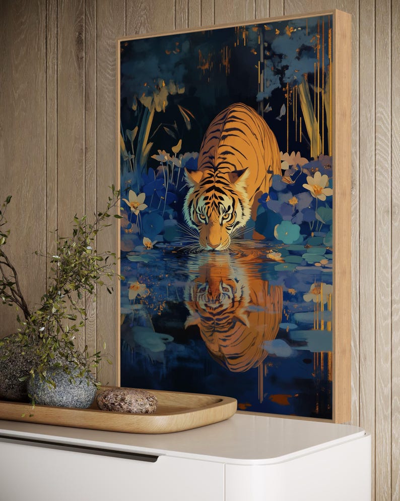 A majestic tiger drinks from a calm lake, its reflection glowing in golden hues. Surrounded by blue flowers and soft light, this art print blends nature with elegance, perfect for boho, nature, or wildlife-themed home decor.