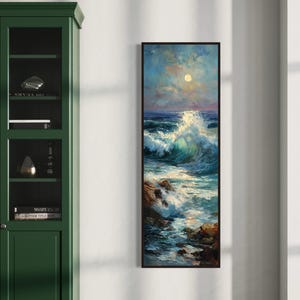 May include: A framed vertical painting depicts a seascape with a crashing wave under a moonlit sky. The artwork features shades of blue, green, and white, with rocky formations in the foreground. The painting is displayed on a white wall.