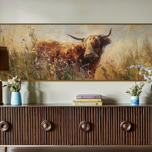 Puede incluir: Una pintura enmarcada de una vaca de las Tierras Altas en un campo de flores silvestres cuelga sobre un mueble de madera oscura. Una lámpara dorada y jarrones con flores están sobre el mueble.