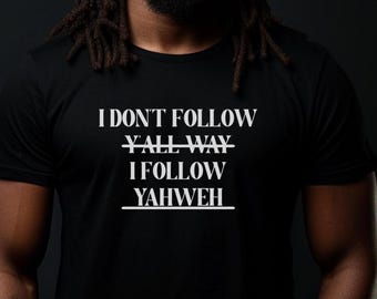 May include: Black t-shirt with white text that reads "I DON'T FOLLOW Y'ALL WAY I FOLLOW YAHWEH". The shirt is short-sleeved and worn by a person with dreadlocks. The background is dark.