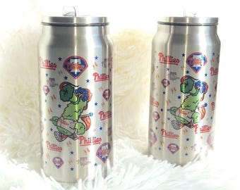 May include: Two stainless steel tumblers with a Phillies baseball team design. Each tumbler features the team logo, the word "Phillies", and a cartoon mascot. The design includes baseballs and stars.