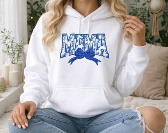 May include: White hoodie with a front pocket and the word "MAMA" in blue floral print. A blue bow design is centered below the word. The hoodie is worn with blue jeans.