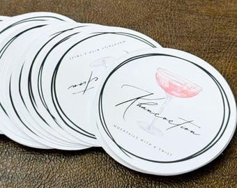 May include: A stack of white round coasters with a black double border. Each coaster features a pink cocktail illustration and the word "Francocction" in cursive. The text "Mocktails with a Twist" is also included.