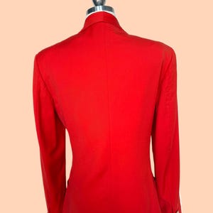 May include: A bright red blazer with long sleeves, displayed on a mannequin. The blazer has a classic design with a notched collar and button details on the sleeves. The back view shows a tailored fit.