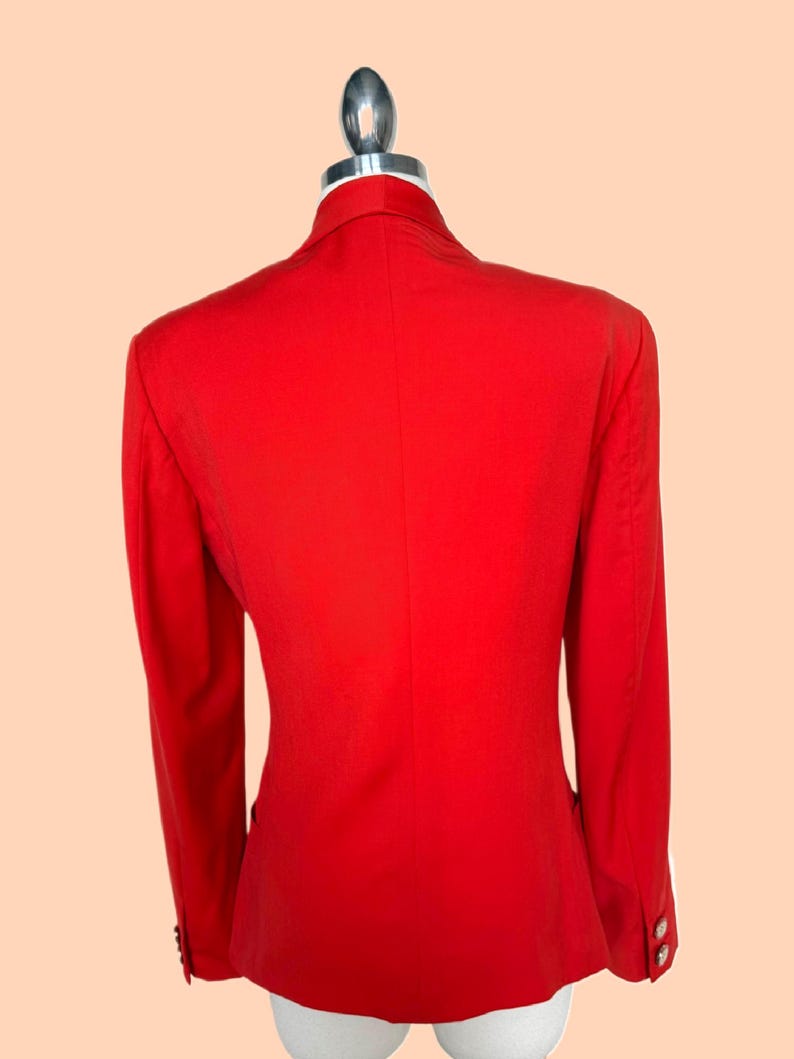 May include: A bright red blazer with long sleeves, displayed on a mannequin. The blazer has a classic design with a notched collar and button details on the sleeves. The back view shows a tailored fit.