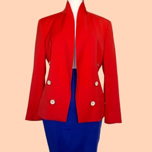 May include: A vibrant red blazer with a unique collar design and four white buttons. The blazer is paired with a royal blue skirt, creating a bold color contrast. The outfit is displayed on a mannequin.
