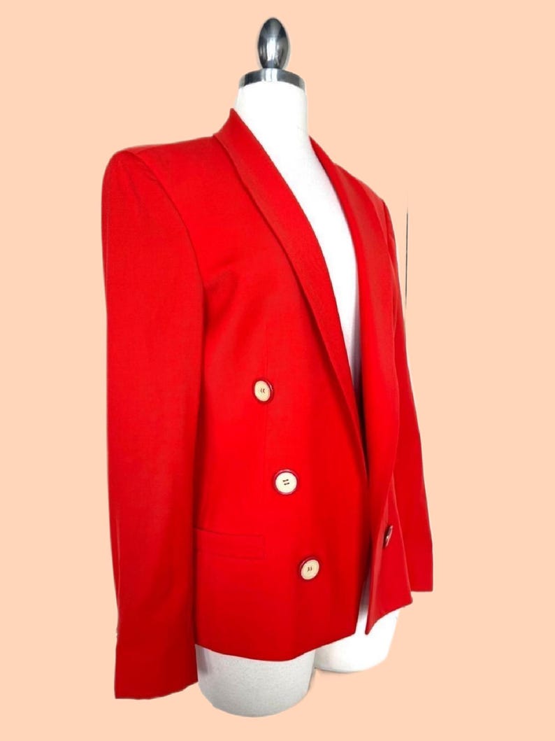 May include: A vibrant red blazer with a classic double-breasted design. The blazer features three white buttons on each side and a notched lapel. The tailored fit and bold color make it a statement piece. The blazer is displayed on a white mannequin.
