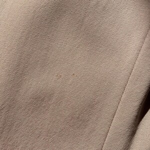 Pu&ograve; includere: Primo piano di una sezione di tessuto beige con una trama a coste diagonali. Il tessuto ha una leggera lucentezza e alcune piccole macchie pi&ugrave; scure. Il bordo del tessuto &egrave; visibile sul lato destro, con una cucitura.