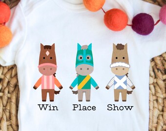 May include: White baby onesie with three cartoon horses wearing jockey silks. The horses are labeled "Win", "Place", and "Show".