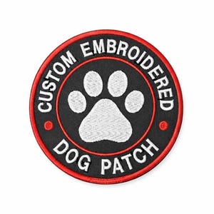 May include: A circular embroidered patch featuring a black background with a white paw print in the center. The text CUSTOM EMBROIDERED DOG PATCH is stitched in white around the paw print, enclosed by a thin red border and a red outer edge.