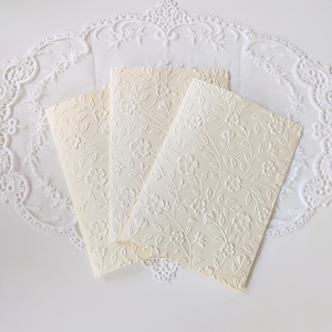 Shows the ivory embossed cards on their own. Front of the card is fully embossed with the floral vine design, creating a textured appearance. Inside of the card shows one blank page for writing the message.